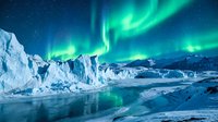 Spectacular aurora borealis dancing over Arctic glacier landscape with icebergs and frozen waters under starry night sky creating magical polar scenery.