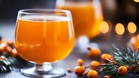 Fresh sea buckthorn juice in glass with raw berries and pine branches on dark background with bokeh lights, healthy vitamin drink for immunity boost.