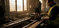 Industrial worker operating machinery in manufacturing facility with natural lighting from windows creating atmospheric workspace environment.