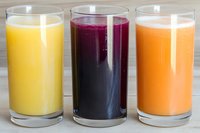 Fresh colorful smoothies in tall glasses on wooden background - yellow pineapple, purple berry and orange carrot drinks lined up for healthy breakfast.