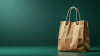 Brown paper shopping bag with handles on dark green background with dramatic lighting and shadow, minimalist composition for commercial and retail design.
