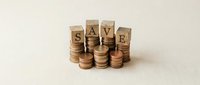 Wooden blocks spelling SAVE surrounded by stacked coins on neutral background representing financial planning and money management concepts.