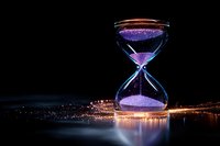 Glowing hourglass with purple sand against night city lights reflecting on water surface, concept of time passing and urban development in modern world.