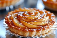 Caramelized apple tart with glazed spiral pattern on flaky pastry crust, served on glass dessert plate, close up view showing golden syrup shine.