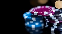Stack of colorful casino poker chips in blue, purple and black on dark background with selective focus and bokeh lights for gambling concept.