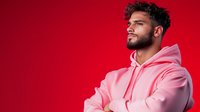 Young Middle Eastern man wearing pink hoodie looking confident against vibrant red background, studio portrait with dramatic lighting and modern urban style.