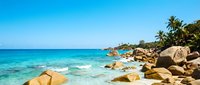 Tropical beach with turquoise water, sandy shore, and large boulders under clear blue sky. Ideal for travel, vacation, and resort marketing materials.