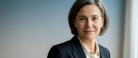 Professional mature businesswoman with short gray hair smiling confidently in dark suit jacket, corporate executive portrait for business presentations.