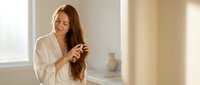 Young woman in white bathrobe combing long brown hair in bright bathroom morning routine self-care wellness lifestyle hygiene beauty ritual daily habits.