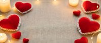 Romantic Valentine's Day background with red velvet hearts, golden lace trim, warm candles and fairy lights on textured fabric surface for love celebration.