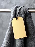 Yellow blank price tag hanging on soft grey towel on metal rod against concrete wall background. Clean minimal composition for spa, bathroom or retail design.