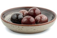 Decorative ceramic bowl with polished spherical balls in deep red and black colors, dusted with white powder on rustic textured pottery background.