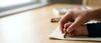 Hand writing with pen on paper notebook at wooden desk in warm natural light for education and business planning.