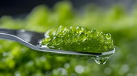 Green caviar on silver spoon with water drop, macro shot against blurred background showing luxurious seafood delicacy in gourmet presentation.
