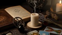 Mystical altar setup with tarot cards, pentagram, burning candle, ancient book and occult symbols for spiritual divination and esoteric practices.