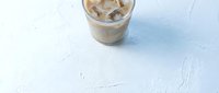 Cold brew coffee with ice cubes in glass on white textured background. Refreshing iced beverage for summer drinks menu and cafe advertising.