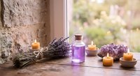 Lavender essential oil bottle with dried lavender bundles and burning candles on wooden windowsill creating peaceful spa atmosphere for aromatherapy relaxation.