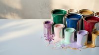 Colorful paint cans with vibrant liquid paint spilling onto white surface creating artistic mess for home renovation and creative projects.