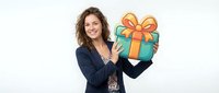 Smiling woman with long wavy brown hair, wearing dark blazer, holding wrapped gift box with gold ribbon against white background for holiday promotions.