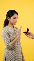 Young South Asian woman refusing marriage proposal with engagement ring on bright yellow background, rejecting commitment and relationship offer.