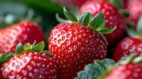 Fresh ripe strawberries with green leaves in macro view showing detailed texture and seeds on bright red berries against natural background.