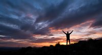 Person with raised arms celebrating freedom against dramatic sunset sky with storm clouds creating inspiring silhouette for motivation and success concepts.