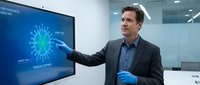 Professional businessman in suit presenting virus data analysis on digital screen in modern office conference room for medical research presentation.