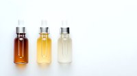 Three essential oil bottles in different shades from dark amber to clear liquid on white background, arranged in gradient order, isolated for cosmetic and wellness projects.