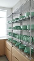 Modern kitchen pantry with chrome wire shelving displaying organized green ceramic dinnerware and dishes for commercial restaurant storage solutions.