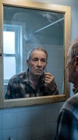 Senior Caucasian man shaving in bathroom mirror wearing plaid shirt. Daily grooming routine, personal care, morning ritual, elderly lifestyle concept.