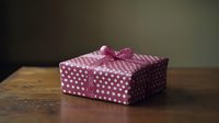 Pink polka dot wrapped gift box with bow on wooden table against dark background, festive present packaging for special occasions and holidays.