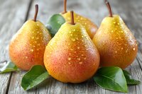 Fresh ripe pears with water droplets and green leaves on rustic wooden background. Healthy organic fruit harvest for cooking and nutrition concepts.