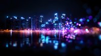 Modern cityscape at night with glowing lights reflecting on water surface, enhanced by vibrant purple and blue bokeh effects in foreground creating dreamy urban atmosphere.