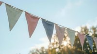Colorful fabric bunting flags hanging outdoors against blue sky with trees in background for party decoration and celebration events.