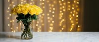 Yellow roses in glass vase on marble table with golden bokeh lights background for romantic home decor and special occasions.
