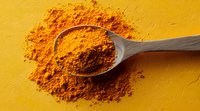 Ground turmeric powder in wooden spoon on yellow background, bright orange spice scattered around, macro food photography for cooking and healthy recipes.