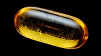 Golden amber oil capsule with suspended particles against black background, showcasing translucent medicinal supplement for health and wellness industry.