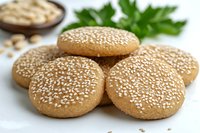 Fresh baked sesame seed cookies arranged on white surface with tahini bowl and parsley garnish for healthy snacking and Mediterranean cuisine recipes.