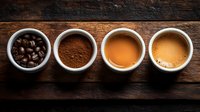 Coffee evolution in white ceramic cups on rustic wooden background: whole beans, ground coffee, brewed espresso, and creamy cappuccino arranged in row.