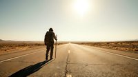 Lone traveler with walking stick on empty desert highway at sunset, journey and adventure concept for travel and exploration themes.