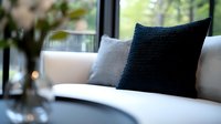 Elegant dark blue textured cushion on white modern sofa near window, soft natural lighting creates cozy atmosphere in contemporary living room interior.