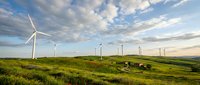 Wind turbines generating renewable energy on green rolling hills under dramatic cloudy sky at sunset. Clean power technology for sustainable future.