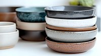 Stacked ceramic bowls in earthy tones of white, gray, brown and teal with speckled textured finish, showcasing modern minimalist tableware design for food styling.