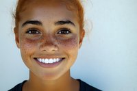 Close up portrait of young woman with freckles and bright smile against light background, natural beauty and authentic expression showing joy and confidence.