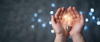 Hands cupping glowing light bulb against dark background with bokeh lights representing innovation, creativity, and bright ideas for business concepts.