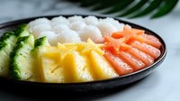Fresh tropical fruit and salmon sashimi arranged in colorful rows with steamed rice on black ceramic plate, served with palm leaf garnish for Asian cuisine.