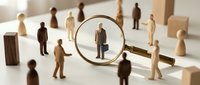 Magnifying glass focusing on wooden businessman figure among crowd of people representing talent search, recruitment, hiring process and human resources management.