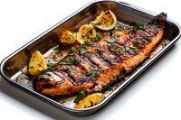 Grilled whole salmon with herbs and lemon slices in roasting pan. Fresh cooked fish dinner with seasoning for restaurant menu and healthy cooking recipes.