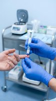 Healthcare professional administering injection with syringe in medical clinic setting with equipment and supplies in background.