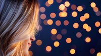 Young blonde woman in profile against blurred golden bokeh lights background, soft focus portrait capturing dreamy evening atmosphere and glowing warm highlights.